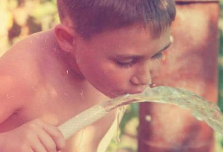 Αγόρι των 80s πίνει νερό από λάστιχο σε αυλή – εικόνα παιδικής ανεμελιάς και απλότητας